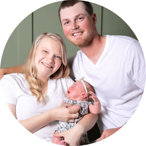 Alison Eddy smiles while holding her baby with husband next to them.